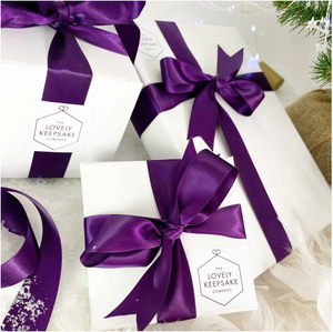 A range of white “Lovely Keepsake Company” presentation boxes, with purple ribbon and logo.