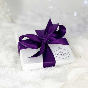 Flattish white “Lovely Keepsake Company” presentation box, with purple ribbon and logo.